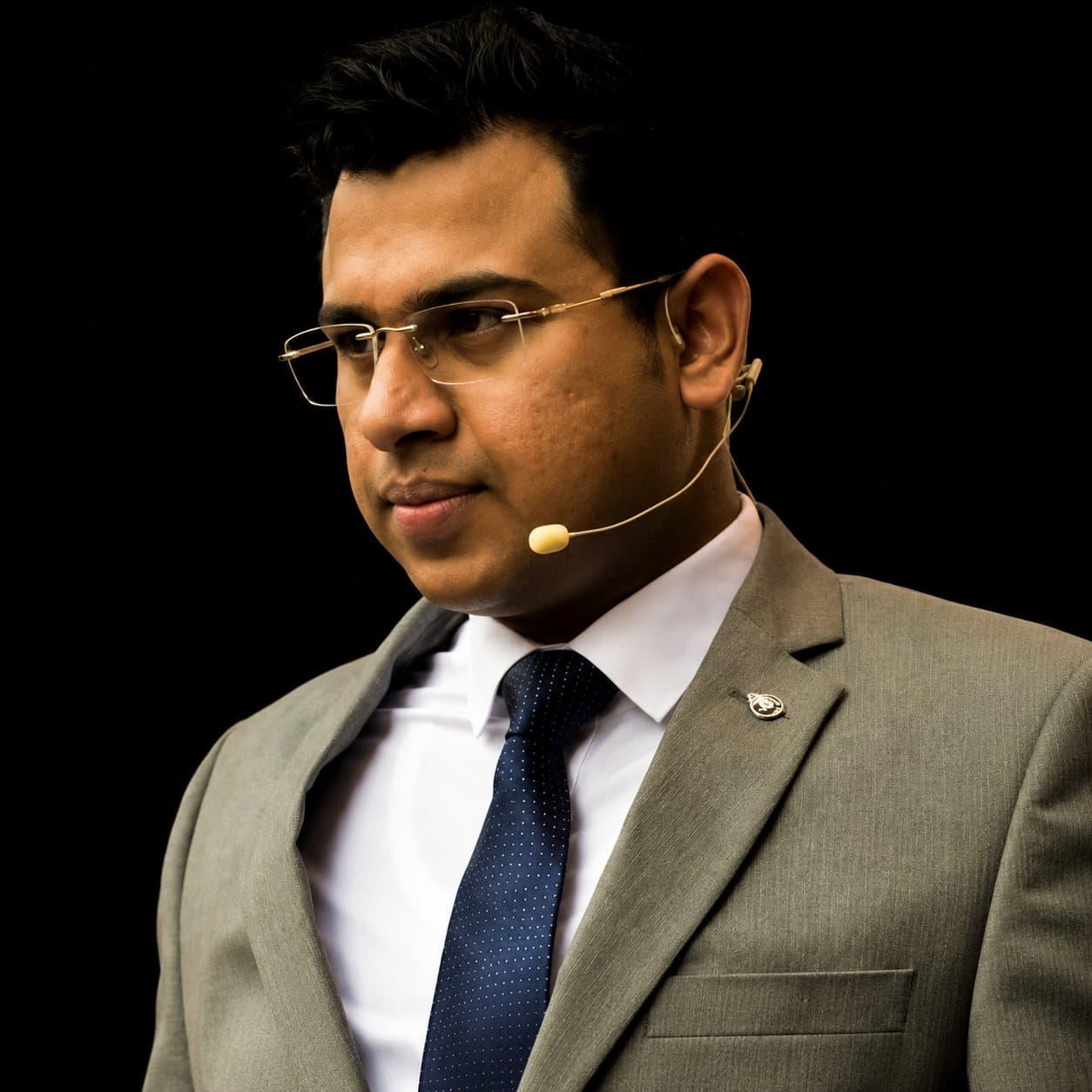 Anmol Pushjai Goel speaking on stage with a headset microphone